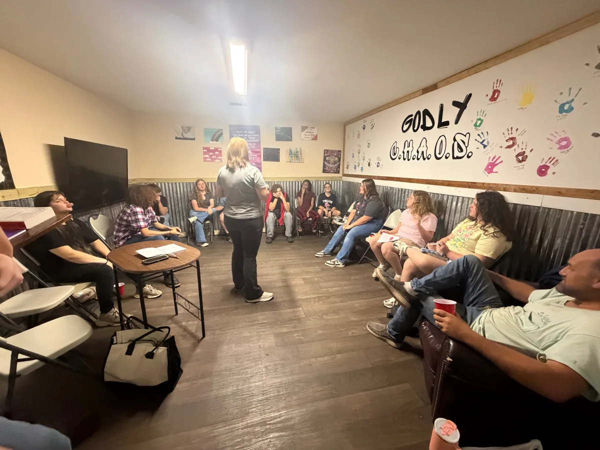 Students sitting in a circle for Wednesday night Bible class in the Godly C.H.A.O.S. room, with a handprint wall