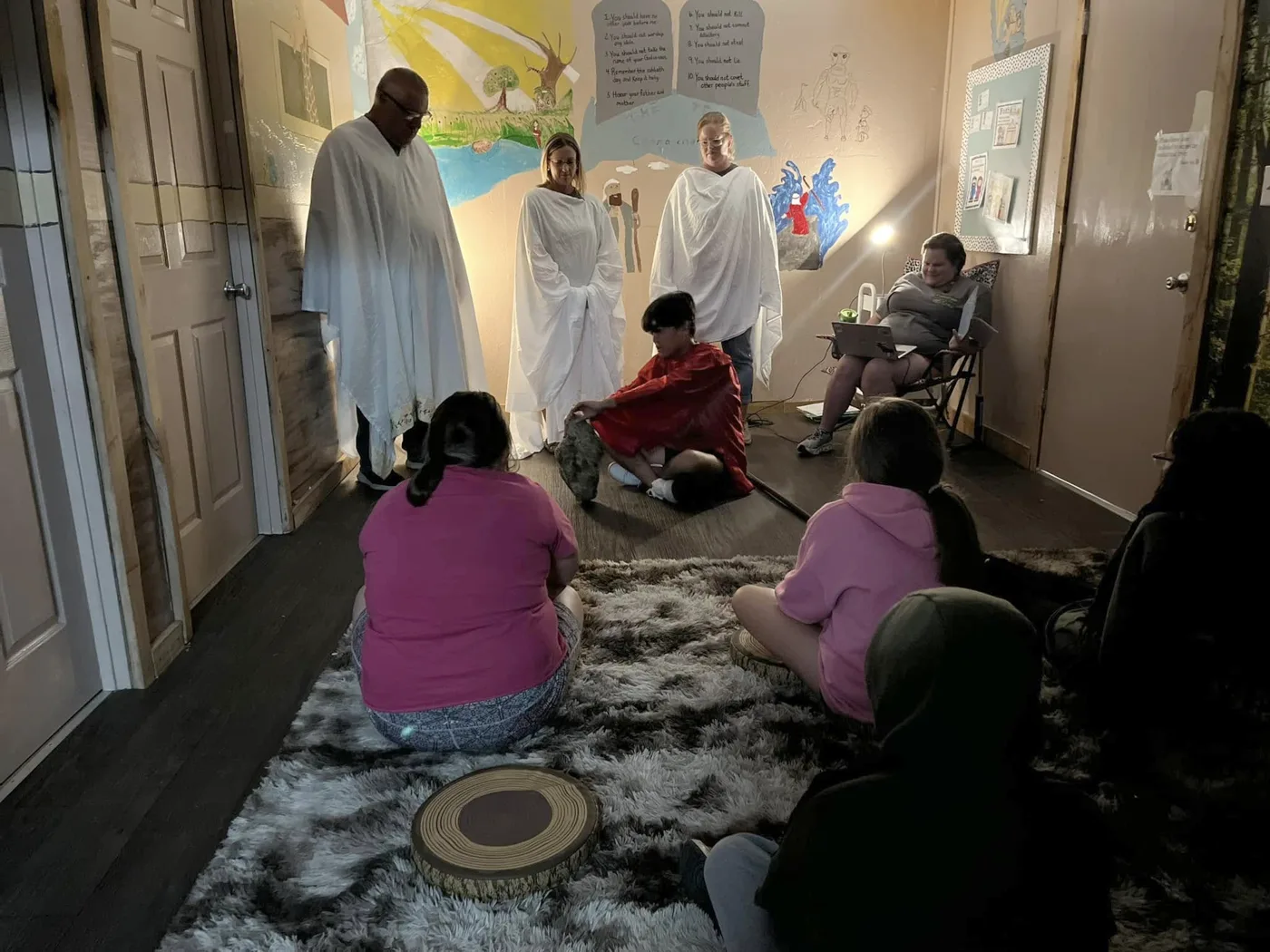 Children sitting on a rug watching leaders in Bible-times costumes act out a Bible story in a Pineview Kids classroom
