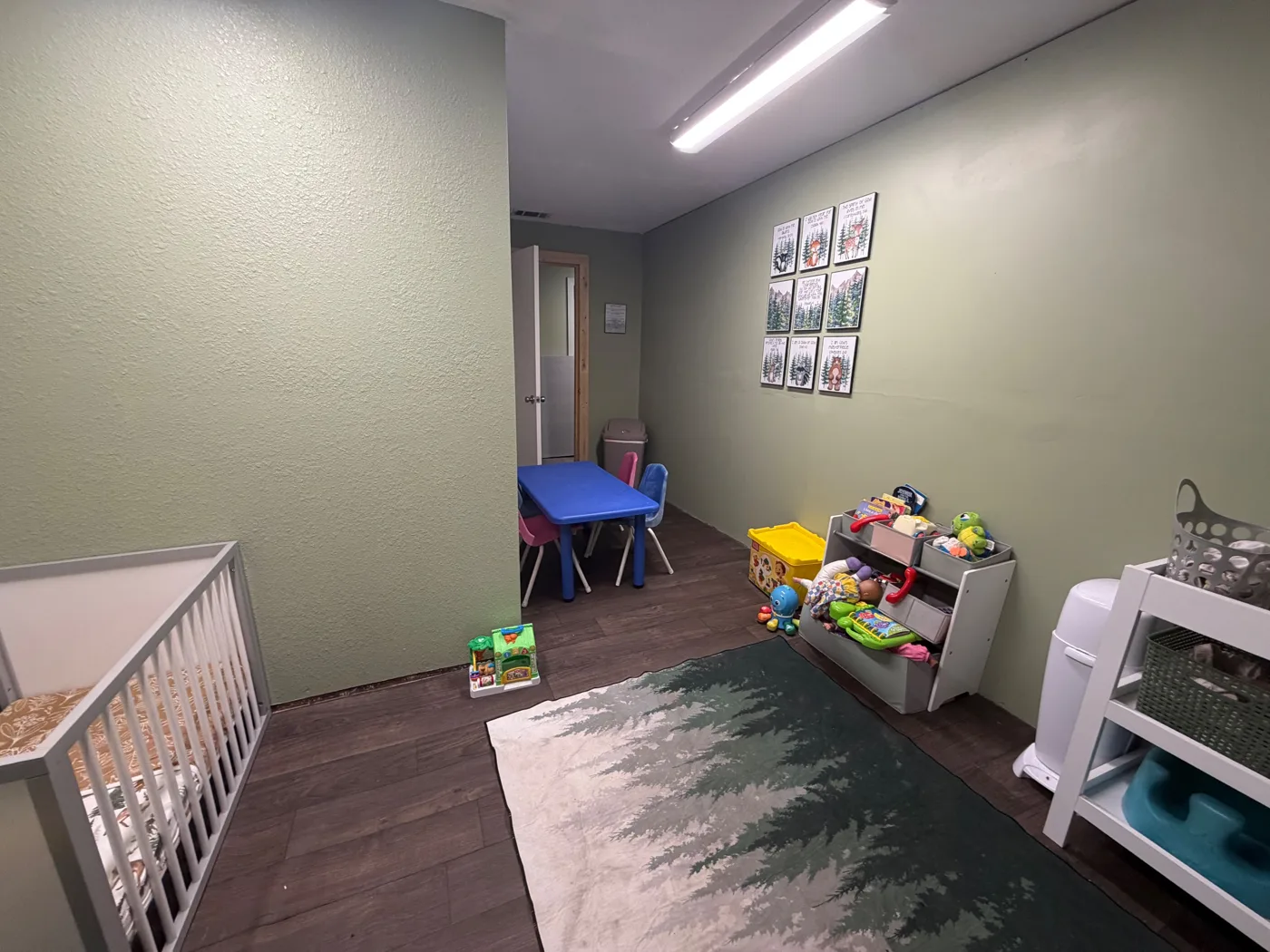 The Pineview Kids nursery with a crib, toys, a pine tree rug and Scripture art on the wall