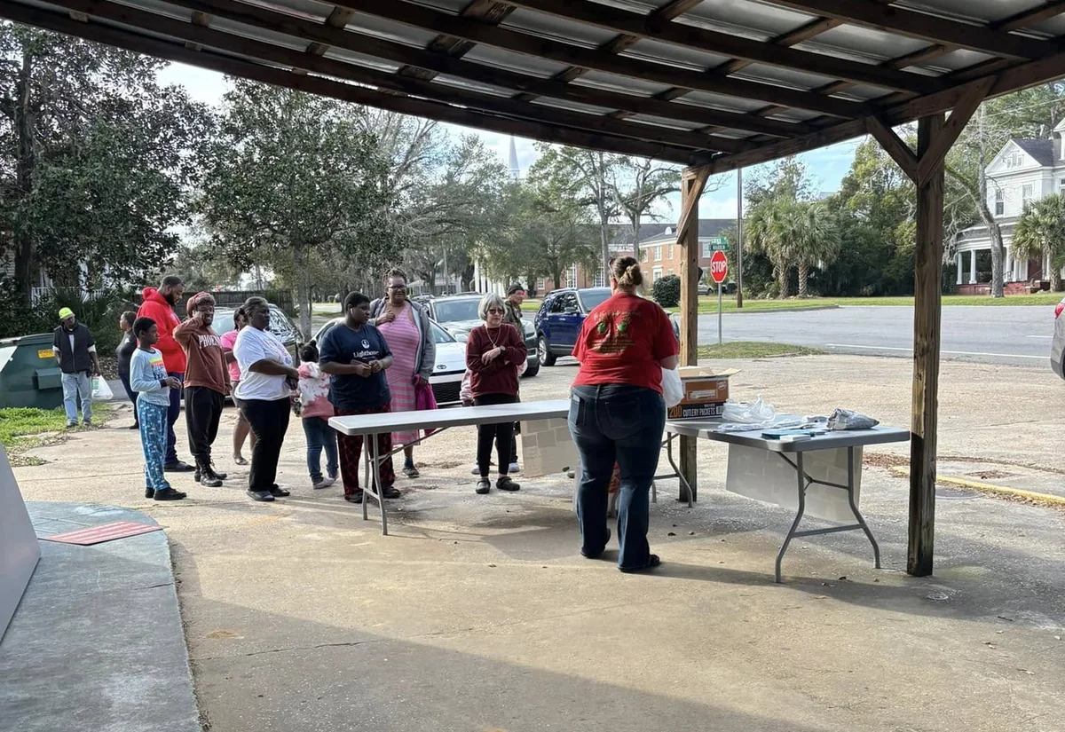 Church volunteers handing out food to neighbors lined up under a covered pavilion